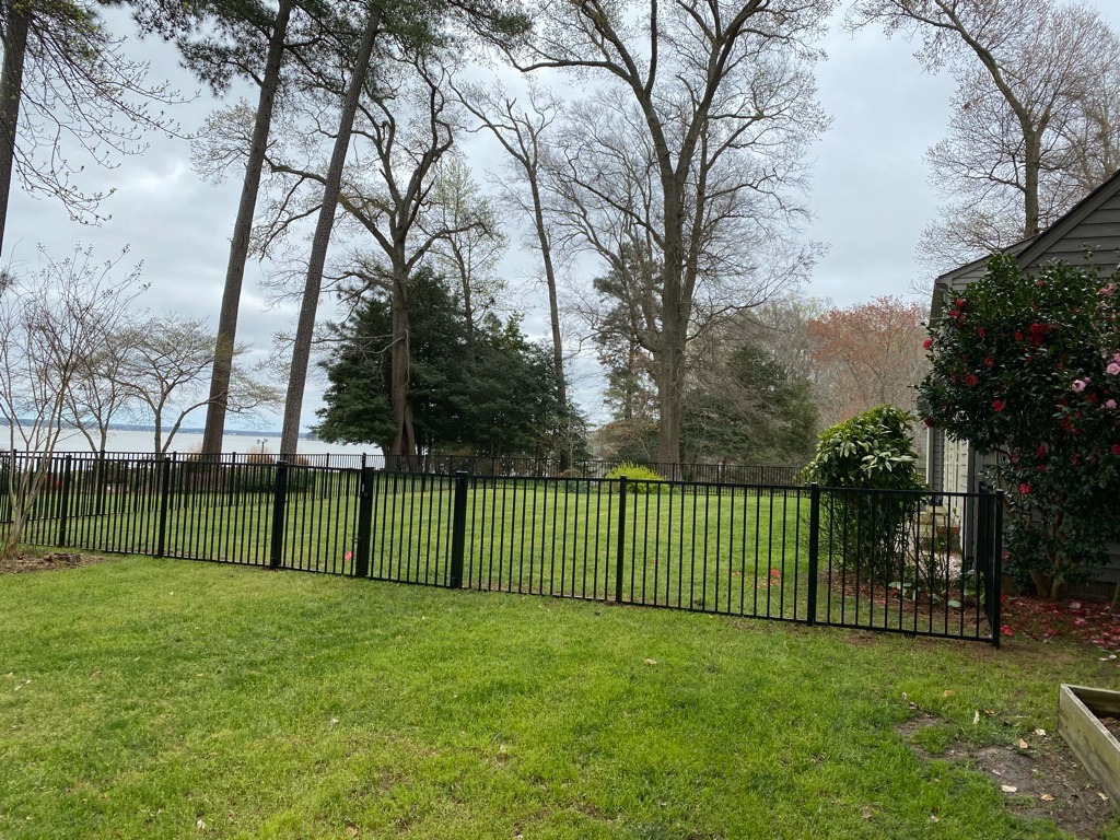 Black aluminum fence enclosing a residential backyard surrounded by tall trees in Dinwiddie, VA.